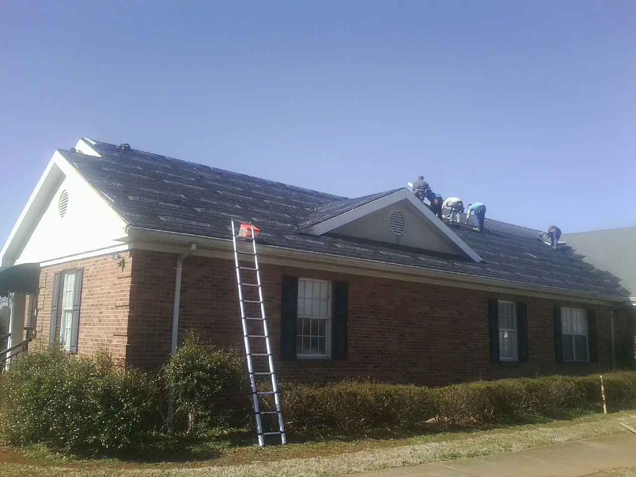 Crew tearing shingles off a brick ranch roof with a ladder set — Metal Roof Repair work by our crew in Paw Paw