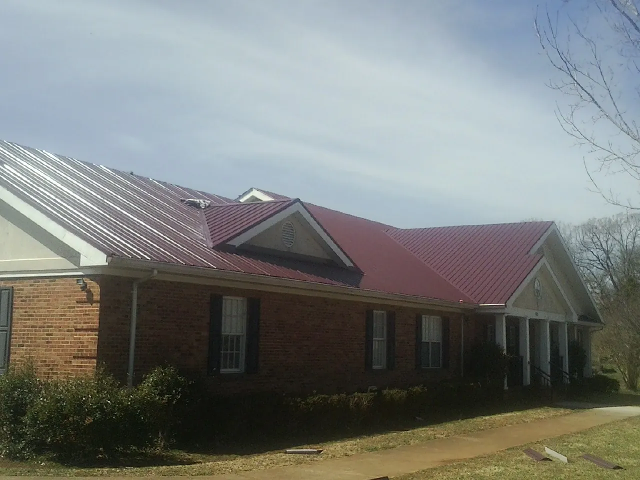 Red metal roof with gabled entries on a long brick building, from a Hail Damage Roof Repair job in Paw Paw
