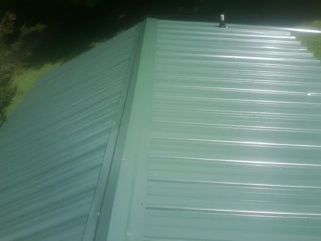 New green metal panels meeting at the ridge of a roof — Flat Roof Repair work by our crew in Paw Paw