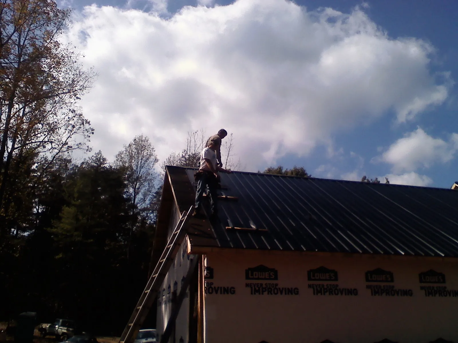 Roofer fastening dark metal panels high against a cloudy sky, from a Roof Inspection job in Paw Paw