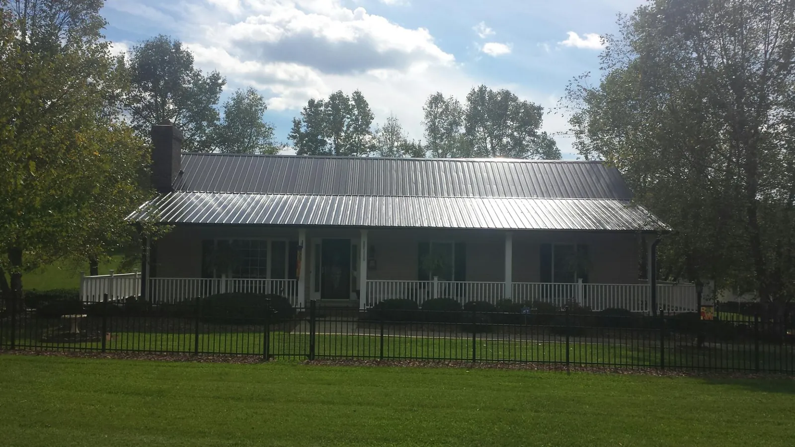 Gray metal roof on a brick ranch with a full width front porch — Gutter Guard Installation work by our crew in Paw Paw