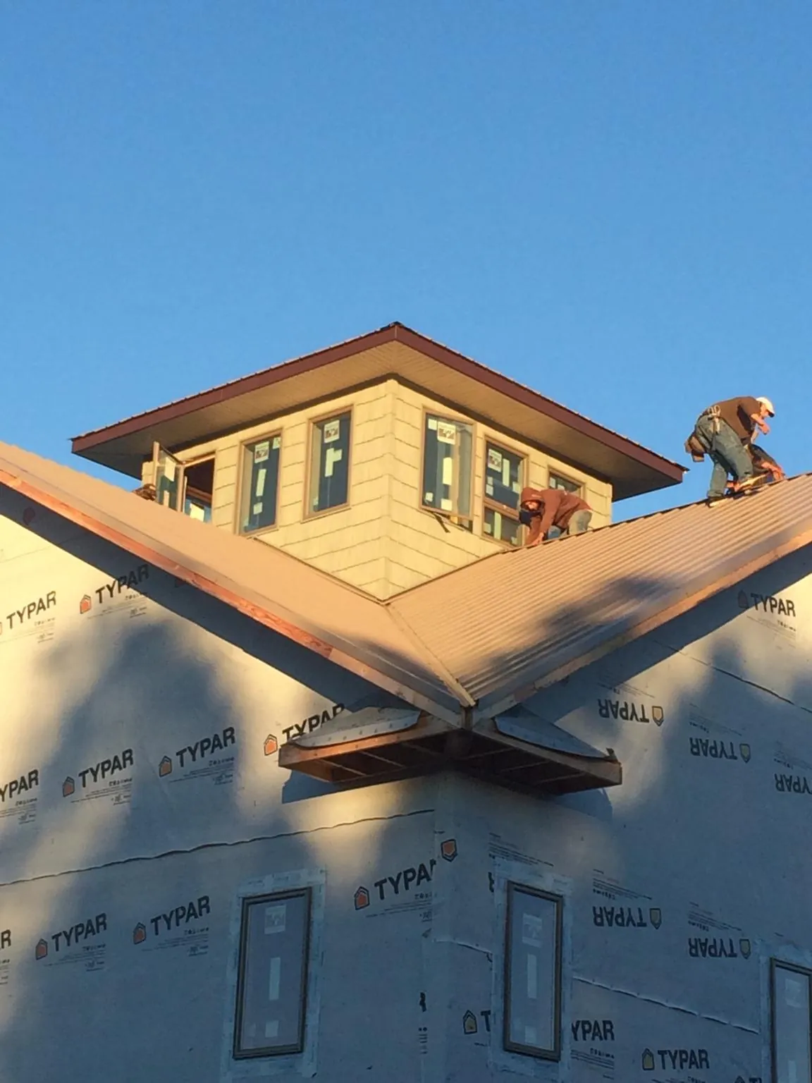 Roofers working around a rooftop cupola on a new metal roof at sunset in Paw Paw